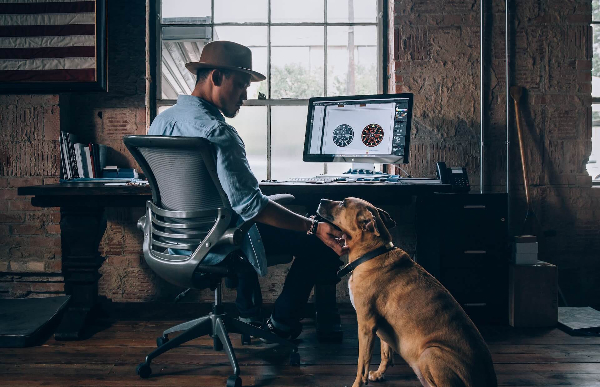 Man sitting on a desk chair scratching a tan dog under the chin.